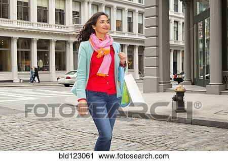 Stock Image - Mixed race woman with shopping bag on city street. Fotosearch