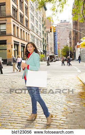 Stock Photograph - Mixed race woman with shopping bag on city street. Fotosearch