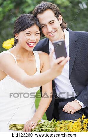 Stock Image - Newlywed couple taking self-portrait at wedding reception. Fotosearch