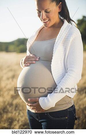 Stock Image - Pregnant Hispanic mother holding stomach in field. Fotosearch
