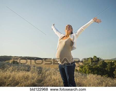 Stock Photo - Pregnant Hispanic mother stretching in rural field. Fotosearch