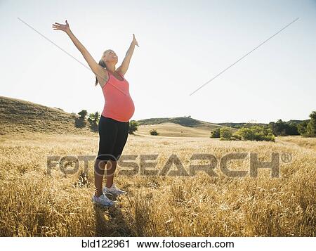 Stock Image - Pregnant Hispanic woman cheering in rural landscape. Fotosearch