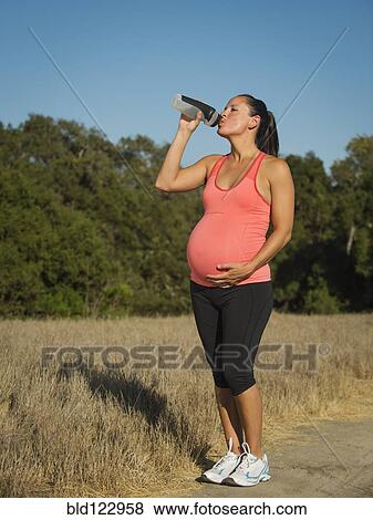 Stock Photo - Pregnant Hispanic woman drinking water outdoors. Fotosearch