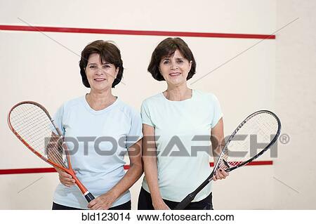 Picture - Senior Hispanic twins holding squash rackets. Fotosearch