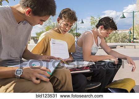 Stock Image - Teenage boys doing homework together outdoors. Fotosearch