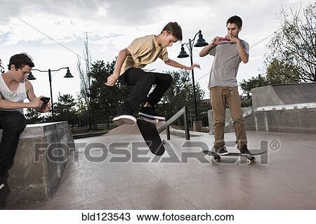 Teenage boys filming each other skateboarding in park View Large Photo Image Stock Image - Teenage boys filming each other skateboarding in park. Fotosearch