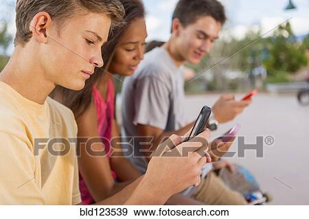 Teenagers using cell phones outdoors View Large Photo Image Stock Photo - Teenagers using cell phones outdoors. Fotosearch