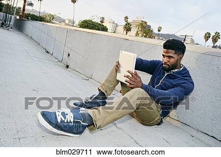 Stock Image - Black man using digital tablet on urban rooftop. Fotosearch