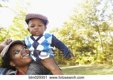 Stock Image - Black mother carrying toddler son in park. Fotosearch