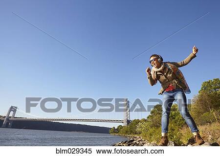 Stock Photography - Black woman listening to headphones at river. Fotosearch