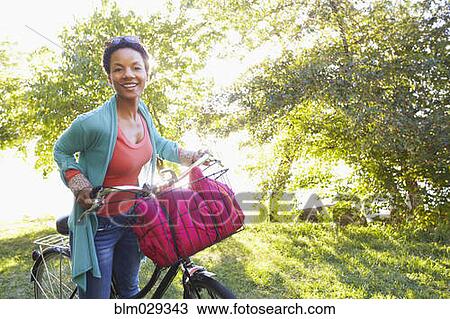 Stock Image - Black woman pushing bicycle outdoors. Fotosearch