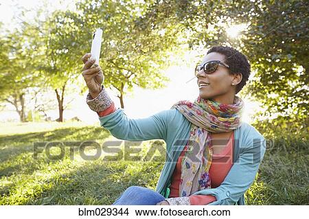 Picture - Black woman using cell phone in park. Fotosearch