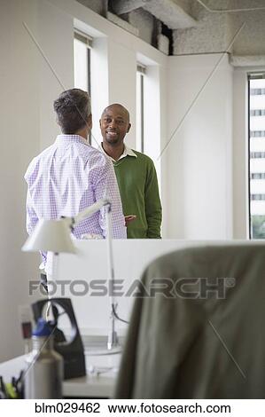 Stock Image - Businessmen shaking hands in office. Fotosearch