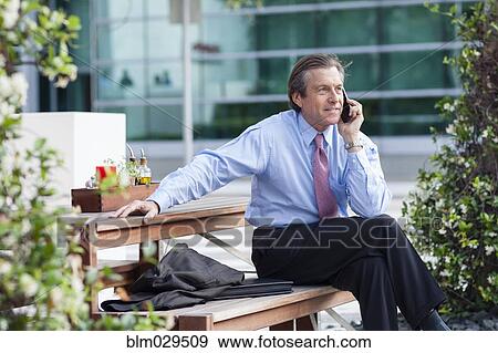 Caucasian businessman on cell phone on picnic bench View Large Photo Image Stock Photo - Caucasian businessman on cell phone on picnic bench. Fotosearch