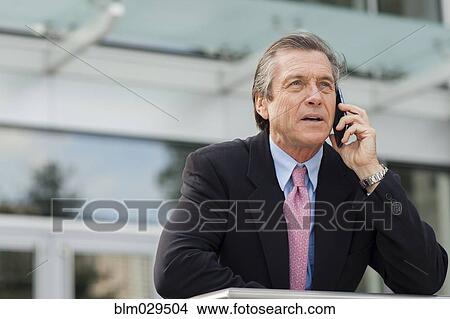 Picture - Caucasian businessman on cell phone outside building. Fotosearch