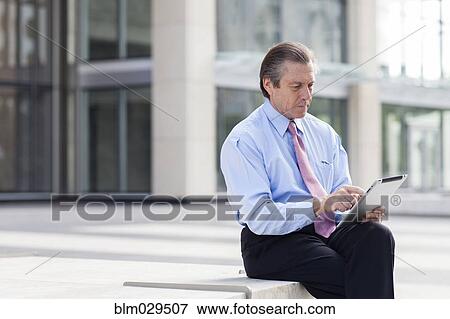 Caucasian businessman using digital tablet in courtyard View Large Photo Image Stock Photo - Caucasian businessman using digital tablet in courtyard. Fotosearch