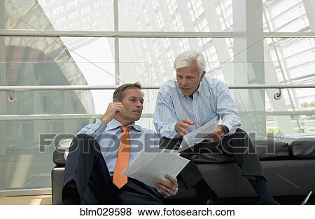 Stock Photo - Caucasian businessmen talking in lobby area. Fotosearch