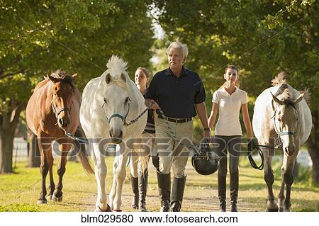 Stock Image - Caucasian family walking horses on dirt path. Fotosearch