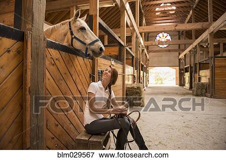 Stock Photo - Caucasian girl sitting with horse in stable. Fotosearch