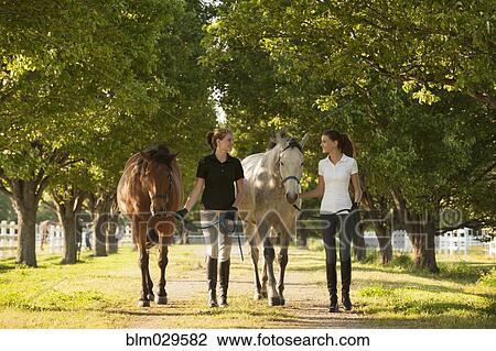 Stock Image - Caucasian girls walking horses on dirt path. Fotosearch