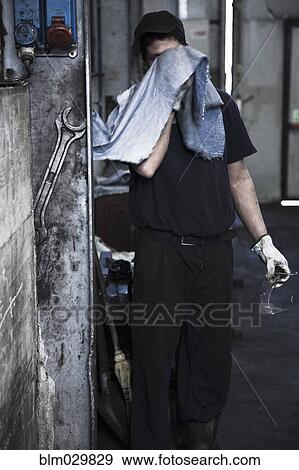 Stock Photo - Caucasian worker wiping his face in factory. Fotosearch