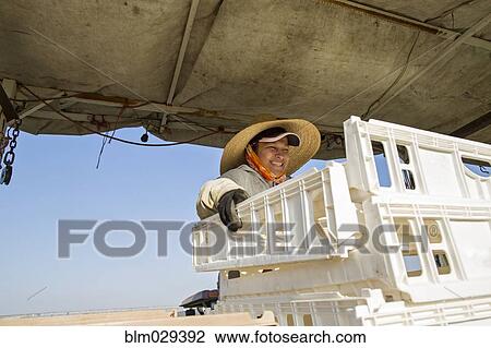 Stock Image - Hispanic farmworker stacking crates in field. Fotosearch