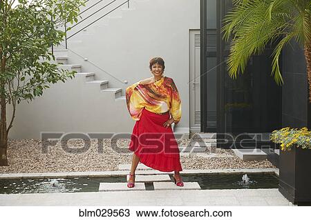 Stock Image - Hispanic woman standing on steps over pond. Fotosearch