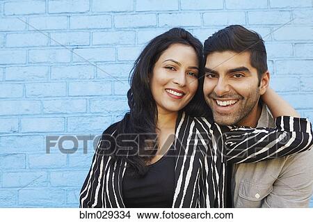 Picture - Indian couple hugging along blue brick wall. Fotosearch