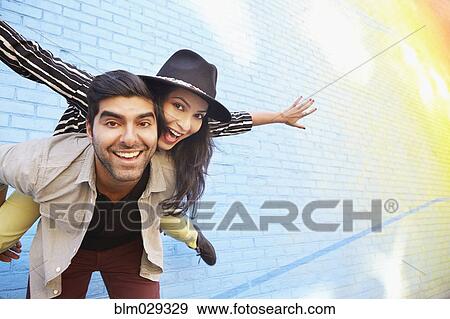 Indian couple piggybacking along brick wall View Large Photo Image Stock Photo - Indian couple piggybacking along brick wall. Fotosearch