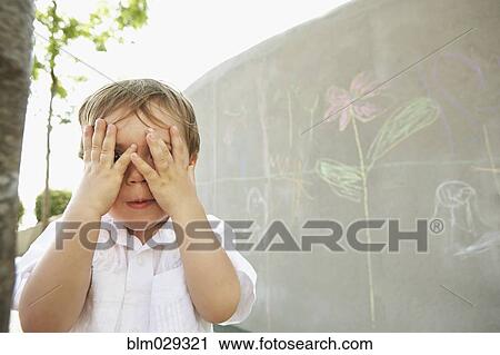 Stock Image - Mixed race boy covering his eyes outdoors. Fotosearch