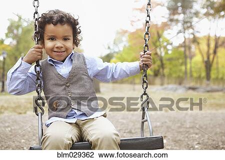 Mixed race boy sitting on swing in park View Large Photo Image Stock Image - Mixed race boy sitting on swing in park. Fotosearch