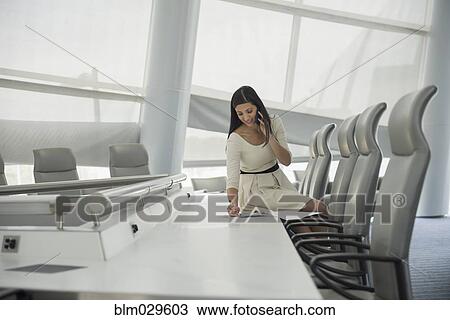 Stock Image - Mixed race businesswoman on cell phone in conference room. Fotosearch