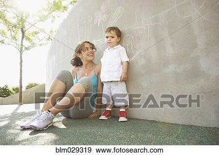 Stock Photo - Mixed race mother sitting with son outdoors. Fotosearch