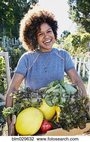 Stock Image - Mixed race woman harvesting vegetables in garden. Fotosearch