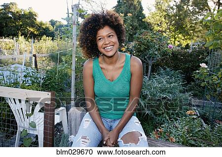 Stock Image - Mixed race woman sitting in garden. Fotosearch