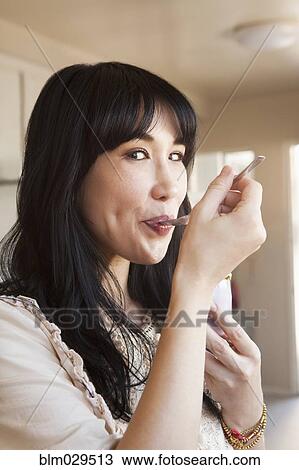 Stock Image - Smiling woman eating in kitchen. Fotosearch