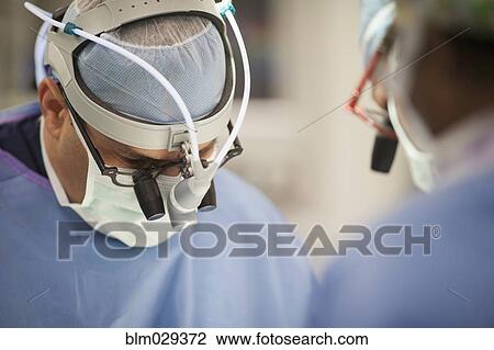 Stock Image - Surgeons wearing magnifying glasses in operating room. Fotosearch