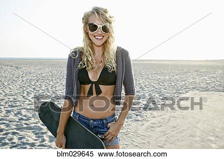 Stock Photography - Woman holding skateboard on beach. Fotosearch