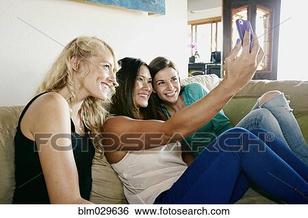 Stock Photograph - Women taking self-portraits together on sofa. Fotosearch