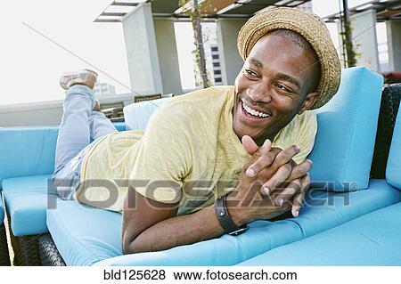 Stock Photo - Black man relaxing on sofa on urban rooftop. Fotosearch