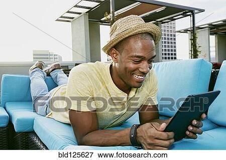 Stock Photo - Black man using digital tablet on sofa on urban rooftop. Fotosearch
