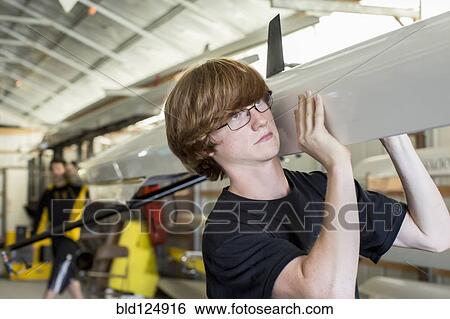 Stock Photograph - Caucasian boy carrying scull in boathouse. Fotosearch