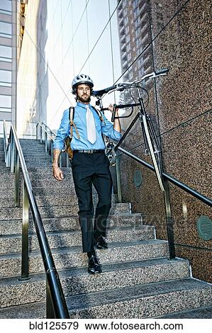Stock Photo - Caucasian businessman carrying bicycle down urban stairs. Fotosearch