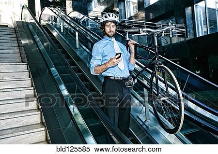 Stock Photography - Caucasian businessman carrying bicycle on escalator. Fotosearch