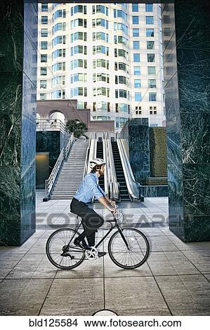 Picture - Caucasian businessman riding bicycle outside highrise. Fotosearch