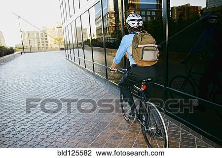 Stock Image - Caucasian businessman riding bicycle outside building. Fotosearch