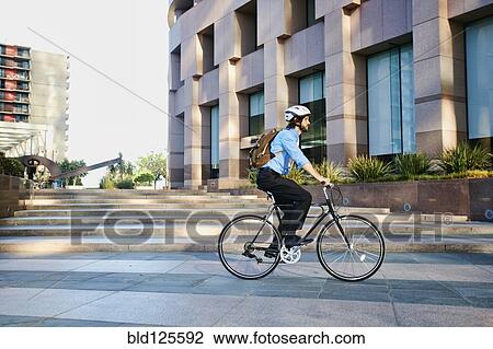 Stock Image - Caucasian businessman riding bicycle outside office building. Fotosearch