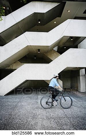 Caucasian businessman riding bicycle outside office building View Large Photo Image Stock Photograph - Caucasian businessman riding bicycle outside office building. Fotosearch