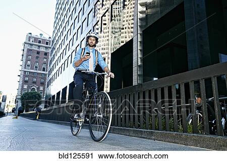 Stock Image - Caucasian businessman using cell phone on bicycle. Fotosearch