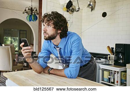 Stock Photo - Caucasian businessman using cell phone in kitchen. Fotosearch